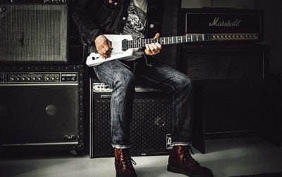 一名男子身穿蓝色牛仔牛仔裤，坐在黑色吉他扩音器上弹奏黑白电吉他